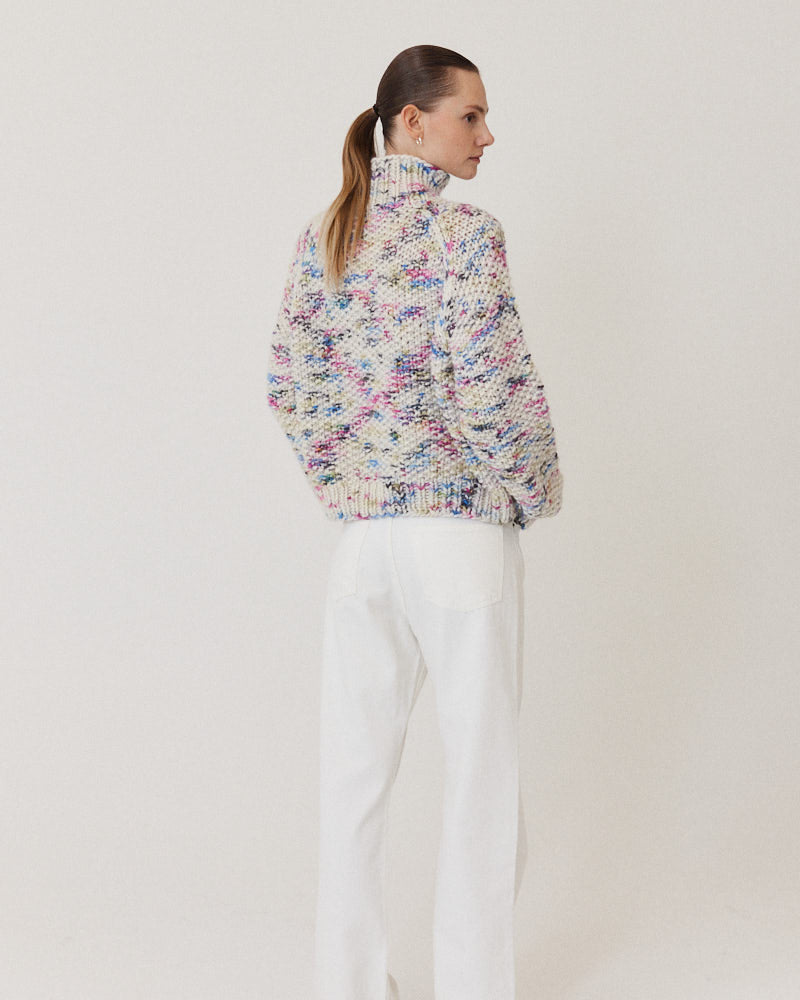 Model wearing structured hand-knitted pullover of merino wool in creme with colorful accents
