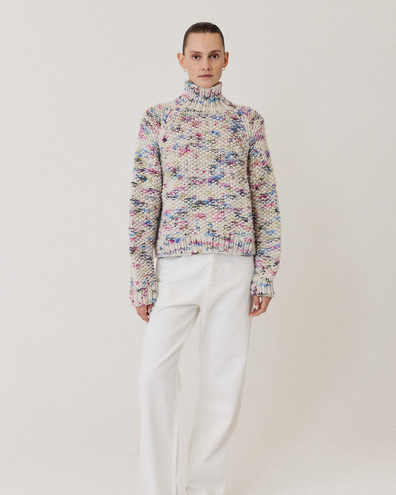 Model wearing structured hand-knitted pullover of merino wool in creme with colorful accents 