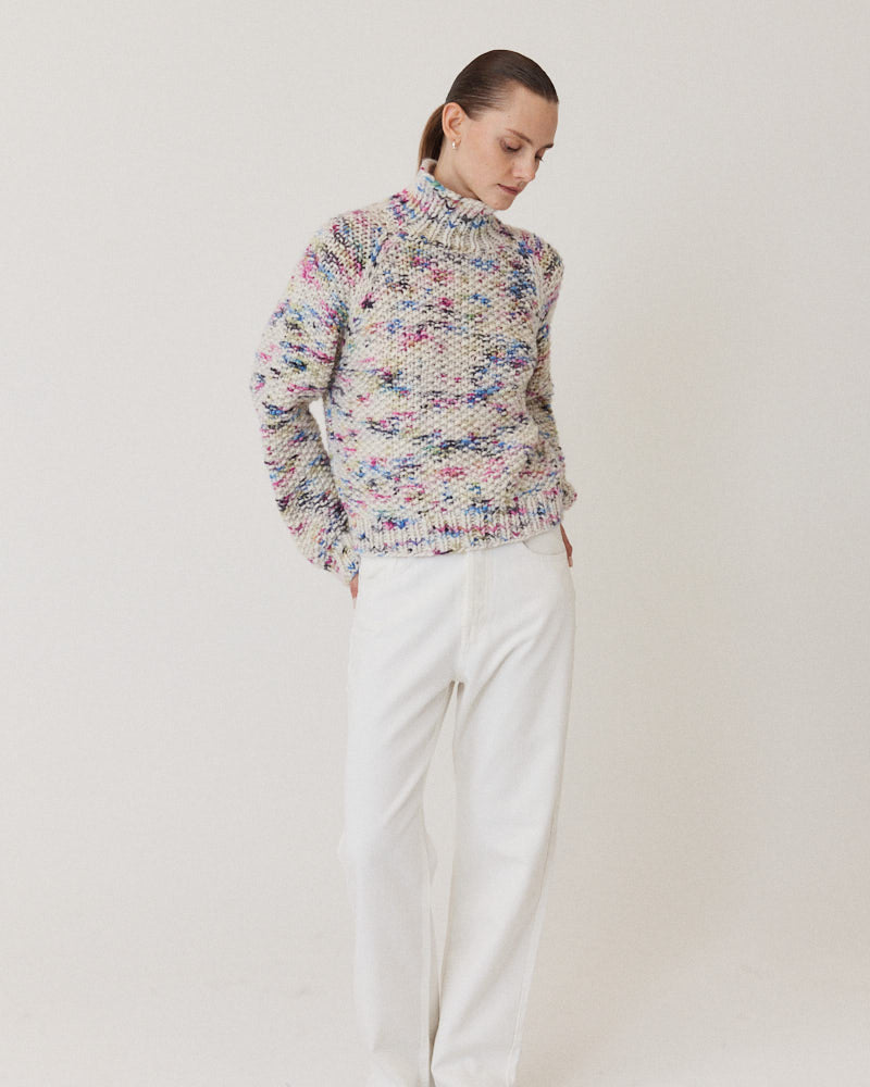 Model wearing structured hand-knitted pullover of merino wool in creme with colorful accents 