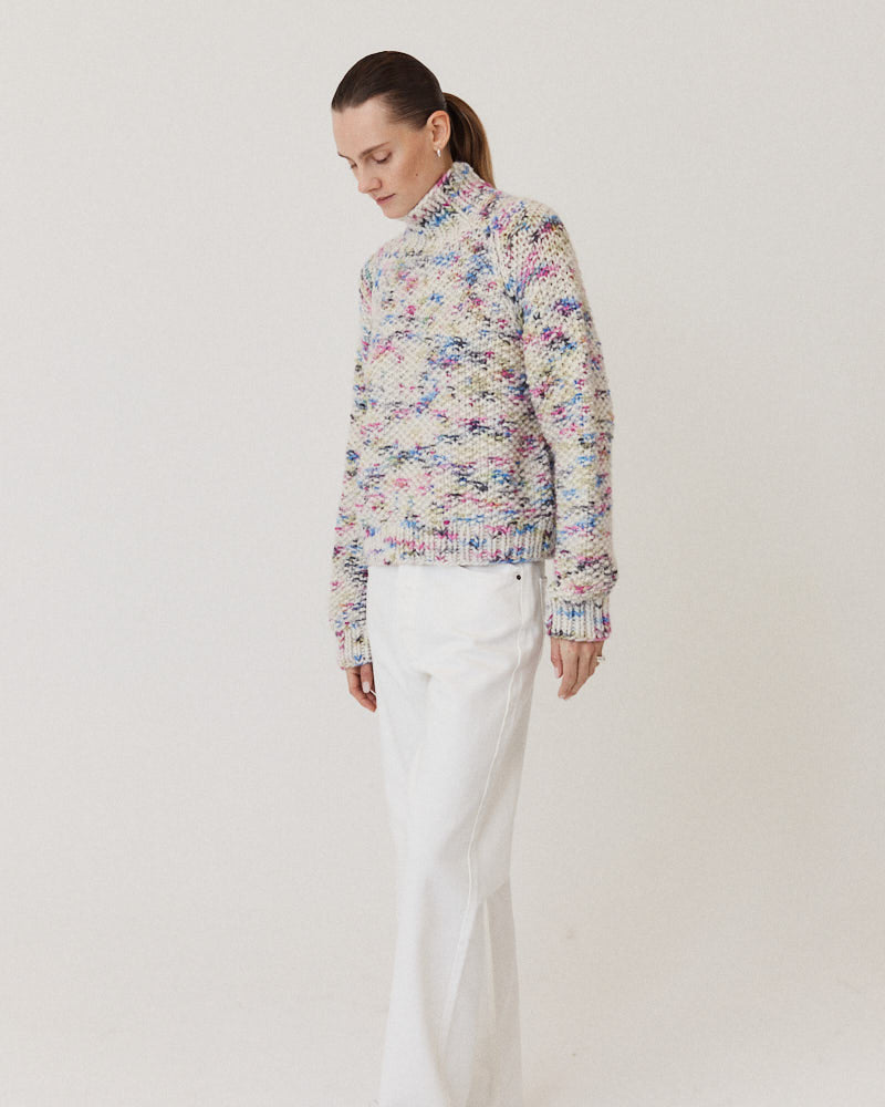 Model wearing structured hand-knitted pullover of merino wool in creme with colorful accents 