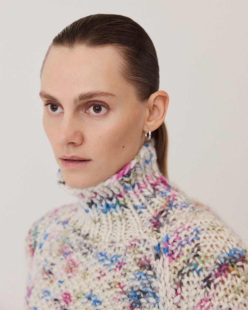 Model wearing structured hand-knitted pullover of merino wool in creme with colorful accents 