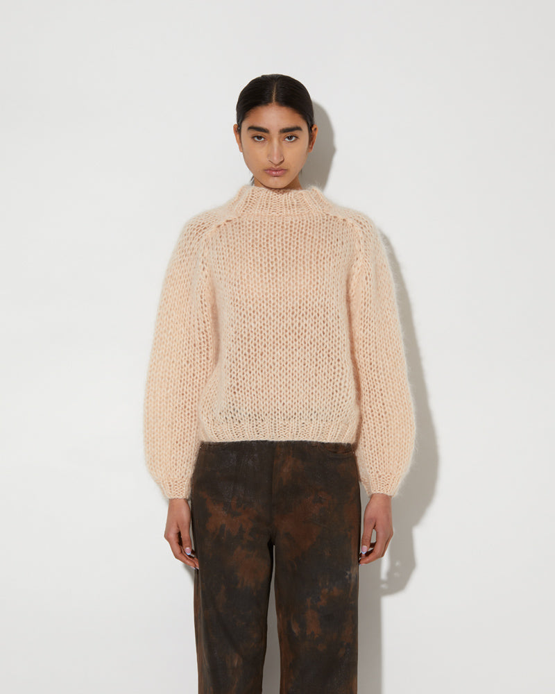 Model wearing a soft mohair textured pullover with airy knit structure and relaxed fit in a light neutral tone