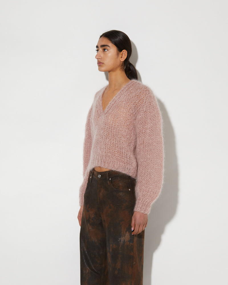 Model wearing a mohair V-neck pullover with soft textured knit and relaxed slightly cropped fit in a muted pink tone