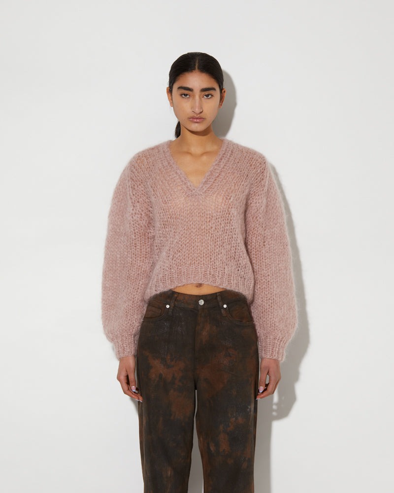 Model wearing a mohair V-neck pullover with soft textured knit and relaxed slightly cropped fit in a muted pink tone